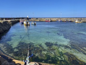 Clear water view of a harbour with small boats surrounded by a stone quay wall, Aberdeenshire,
