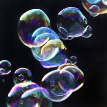Iridescent soap bubbles in the colours of the rainbow against a black background, Recklinghausen,