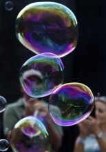 A man and a woman photograph iridescent soap bubbles in front of a black background,