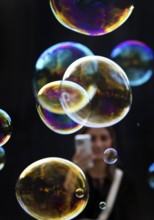 A woman photographs shimmering and floating soap bubbles against a black background,