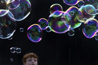 A boy marvels at shimmering and floating soap bubbles against a black background, Recklinghausen,