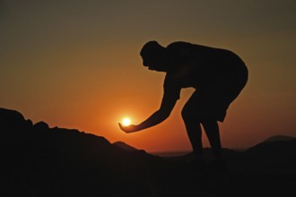 A silhouetted man holds the setting sun in his hand, Namibia