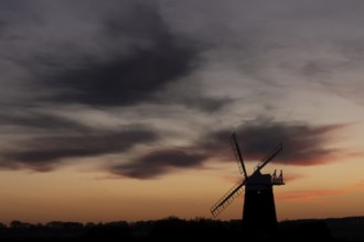 Windmill silhouette at sunset with a red sky and dark clouds, Burnham Ovary Staithe, Norfolk,