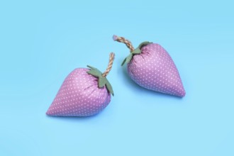 Two handmade pink fabric strawberries on blue background as creative DIY decoration