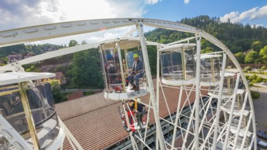 Workers on a platform of a Ferris wheel, surrounded by forest and sky, fire brigade exercise for
