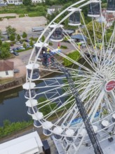 Workers working on a Ferris wheel near a river and building, fire brigade exercise for gondola