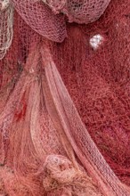 Colourful fishing nets in shades of red that create an interwoven, textured surface, Croatia