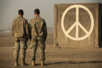 Two soldiers facing painted peace symbol on brick wall. Contrast between duty and hope in times of