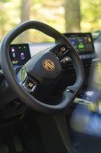 Modern tech displays and steering wheel in the car interior, forest and sunlight in the background,