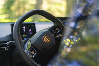 Close-up of the steering wheel and the screens in the car, trees and light in the background, MG 4,