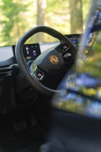 Interior of a car with focus on the steering wheel and digital displays, background of trees, MG 4,