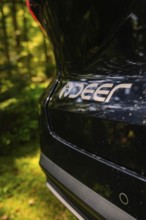 Close-up of the brand logo on the rear of a black car, surrounded by natural forest, MG 4, Deer E-