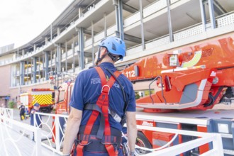 Fire brigade employee with protective helmet looking at a red fire engine, fire brigade exercise