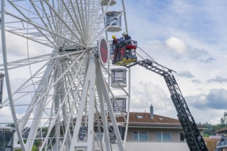 Firefighters during rescue work on a Ferris wheel with residential buildings in the background,