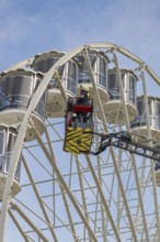 Fireman in the rescue cage is lifted to the cabins of the Ferris wheel, blue sky as background,