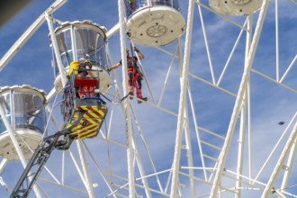 Firefighters at work on a high Ferris wheel under a blue sky, Fire brigade exercise for gondola