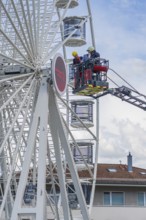 Firefighters in the rescue cage near the Ferris wheel, a building is visible in the background,