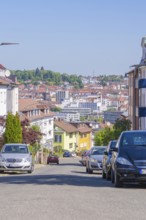 View of a city street with parked cars and background buildings under a blue sky, Pforzheim,