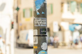 A lamppost with graffiti and stickers in an urban environment with a blurred background, Merano,