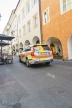 An ambulance drives through a historic old town with orange and yellow colours, Merano, South