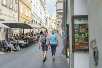 Couple walking through a pedestrian zone with restaurants in the background, mountain view in