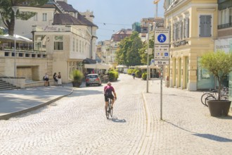 Biker riding through sunny cobblestones in a lively town, Merano, South Tyrol, Italy