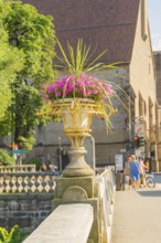 Stone bridge with flower pot, church and pedestrians in the background, Merano, South Tyrol, Italy