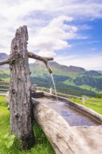 A rustic wooden fountain with running water in a picturesque mountain landscape, Zallinger Alm,