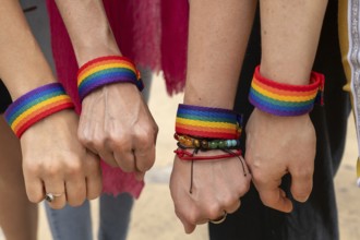 Four hands adorned with vibrant rainbow bracelets are forming fists, representing solidarity and
