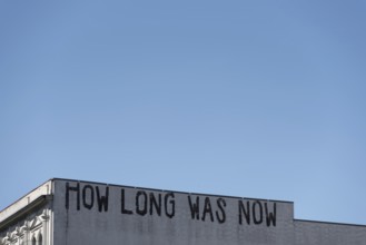 The lettering HOW LONG WAS NOW is emblazoned on the faÃ§ade of a building in Berlin-Mitte, Berlin,