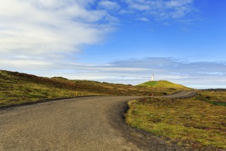 Winding tarmac road leads through barren volcanic landscape, Reykjanesviti lighthouse on the