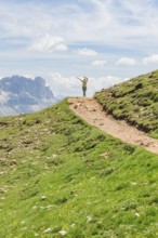 Person hiking on a path with views of rocky mountains and wide skies, Schlehrn hike, Alpe di Siusi,