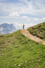 Hikers on a path in a mountainous landscape under a blue sky, Schlehrn hike, Alpe di Siusi,