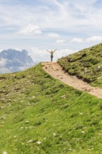 Person opens his arms on a hill path with a view of rocky mountains, Schlehrn hike, Alpe di Siusi,