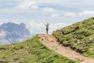 Person spreading his arms on a path in front of a majestic mountain scenery, Schlehrn hike, Alpe di