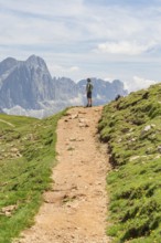 Hiker standing on a path with visible rocks and imposing mountains, Schlehrn hike, Alpe di Siusi,