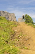 A hiker walks along a sunny nature trail, surrounded by mountainous landscape, Schlehrn hike, Alpe