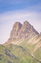 Barren rock towers into the clear blue sky, surrounded by gentle green slopes, hike to the