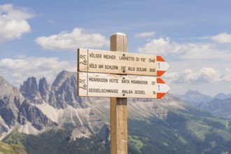 Wooden signpost with directions, mountain panorama in the background under a clear sky, hike to the