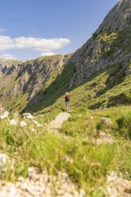 Person hiking on a path between steep slopes, green nature and blue sky, hike to the Schlehrn,