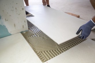 Tile laying: Tiler lays large light-coloured floor tiles