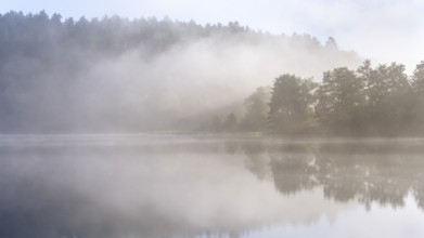 Lake Blaibach on a misty morning. Atmospheric reflection with clouds. Blaibach, district of Cham,