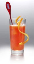 Campari cocktail in a long drink glass on ice with orange zest as garnish against a white