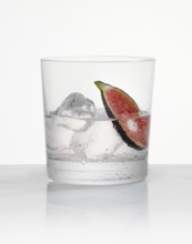 White rum in a tumbler on ice with a fig slice as garnish against a white background, studio shot