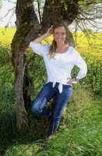 Young woman standing at an old willow tree in SkÃ¥ne County, South Sweden
