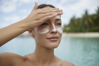 Woman applying sunscreen to her face. Soft-focus beach portrait evoking summer warmth and sun