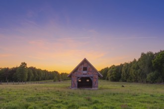 View of an open half-timbered barn standing on a pasture in the sunset, meadow, spring, awakening,