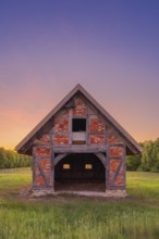 View of grasses and an open half-timbered barn standing on a pasture in the sunset, meadow, spring,