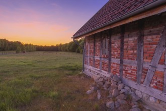 View along an outer wall of a half-timbered barn standing on a pasture in the sunset, meadow,