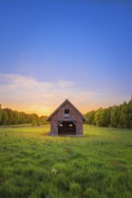 View of an open half-timbered barn standing on a pasture in the sunset, meadow, spring, awakening,